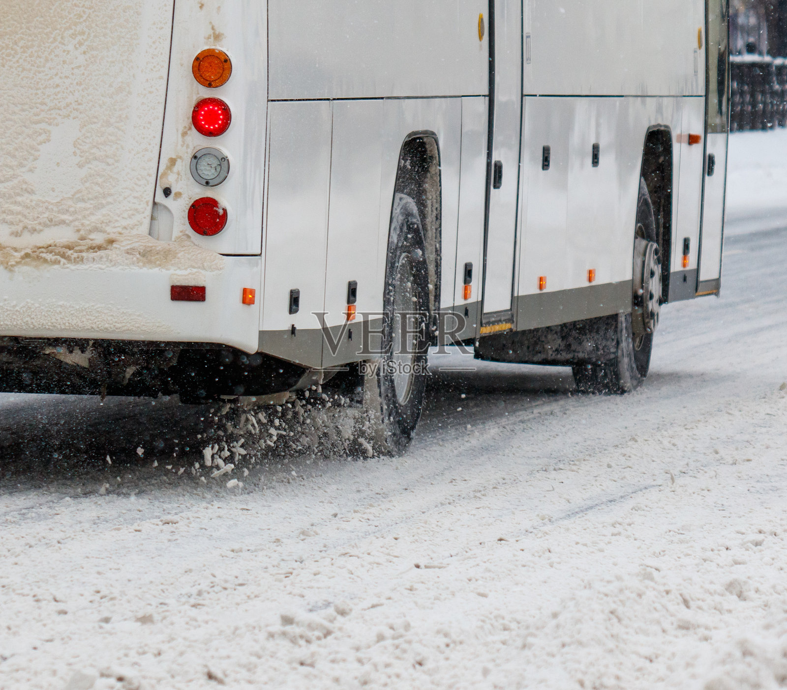 一辆公交车在雪-covered的道路上行驶，车灯亮着。照片摄影图片