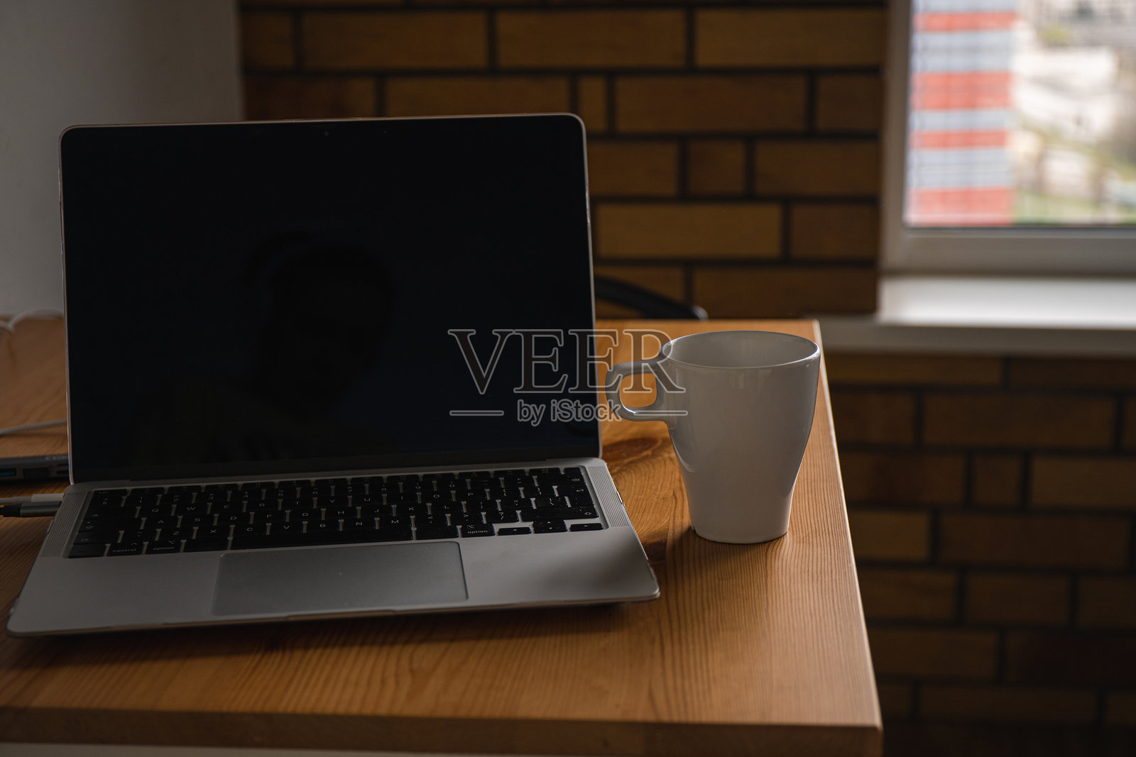 简约的工作空间，窗边的木桌上放着一台笔记本电脑和一杯咖啡。小公寓。照片摄影图片