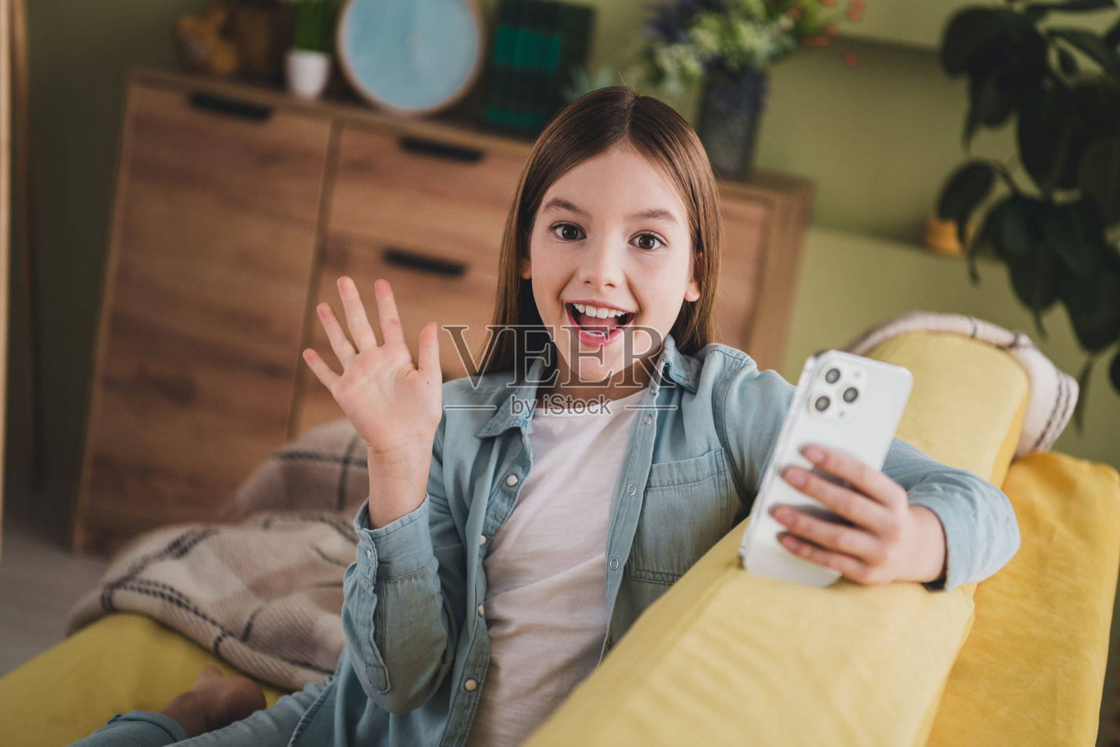 可爱的年轻女孩穿着休闲牛仔服，在明亮的室内拿着手机，表达兴奋和快乐，悠闲地放松。照片摄影图片