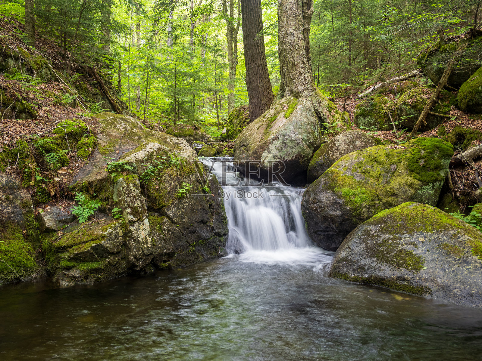 一条小溪在纽约州阿迪朗达克山脉的湖泊平静外的大石头之间流淌。照片摄影图片