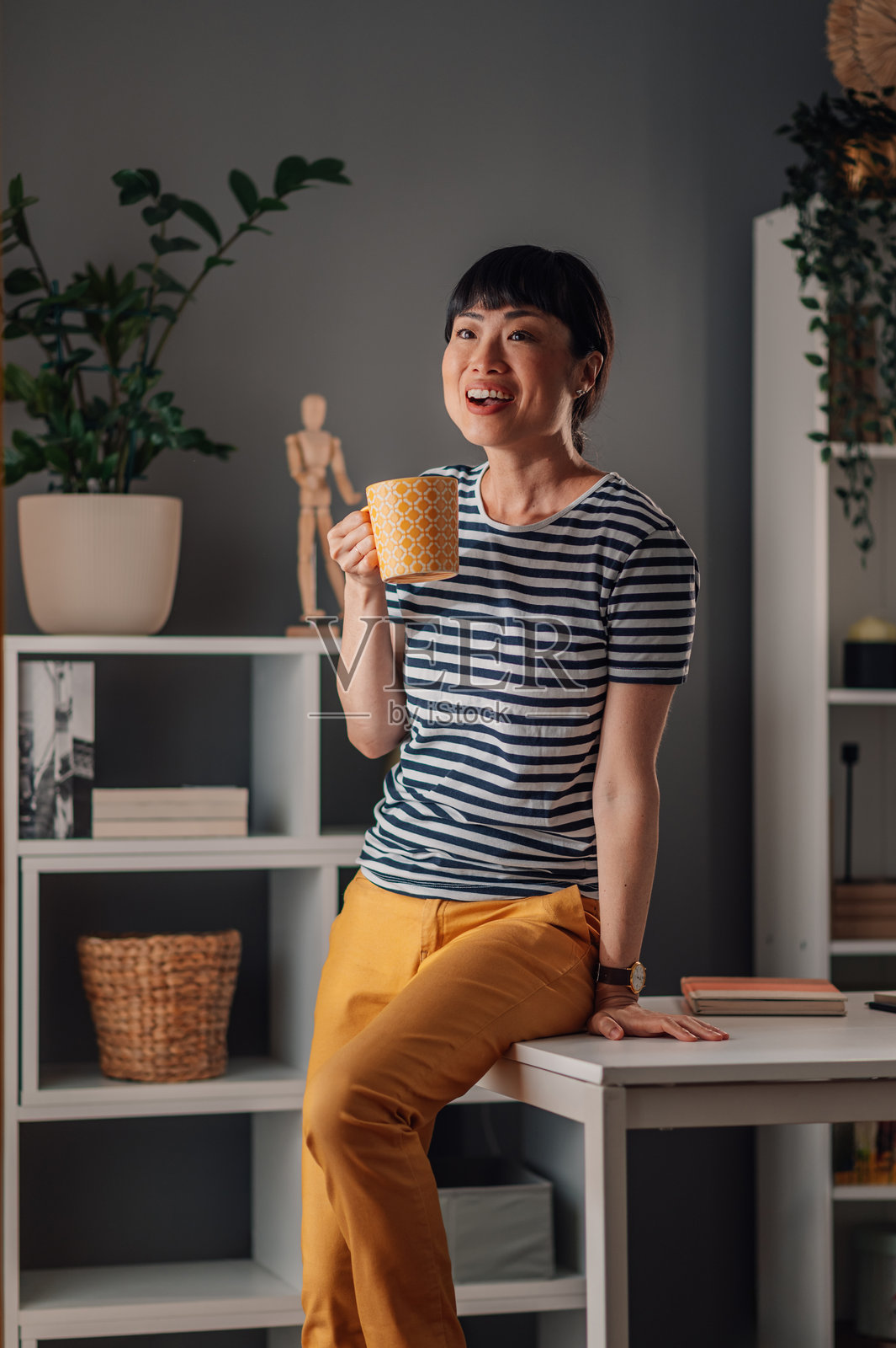 亚洲女性在家办公室微笑，享受窗边的咖啡休息时光。照片摄影图片