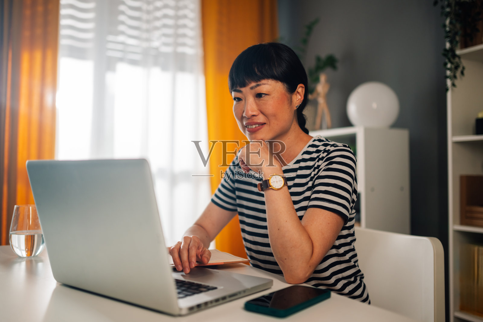 亚洲女性在光线充足的家庭办公室里认真工作，使用笔记本电脑。照片摄影图片