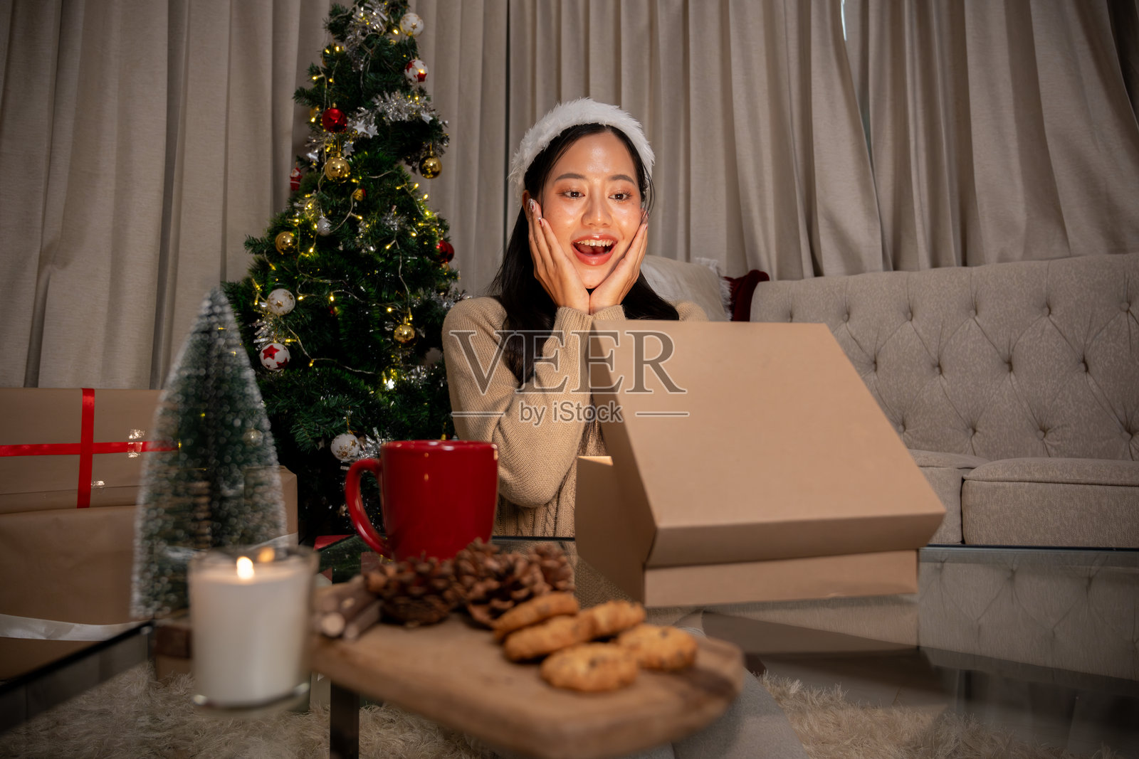 穿着棕色毛衣的亚洲女性在客厅兴奋地打开礼物盒照片摄影图片