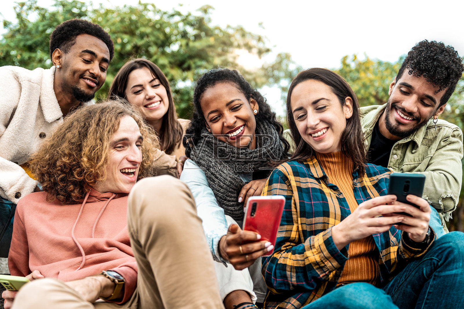 一群多种族的年轻人在户外使用智能手机 - 快乐的大学生们坐在校园里观看手机 - 青少年沉迷于社交媒体科技照片摄影图片