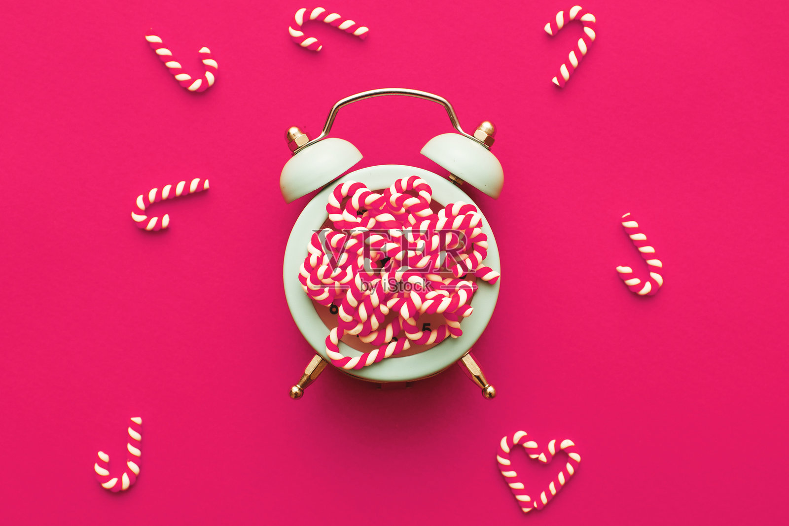 粉色背景上的闹钟上放着圣诞糖果棒的背景图照片摄影图片