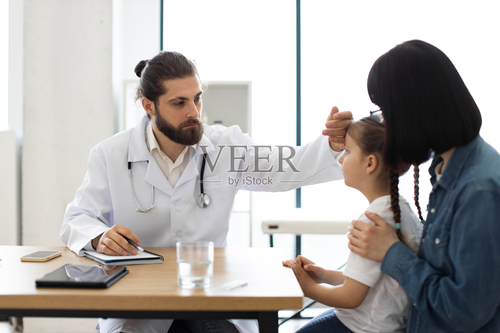 医生在诊所检查孩子的体温，母亲在旁观察。照片摄影图片