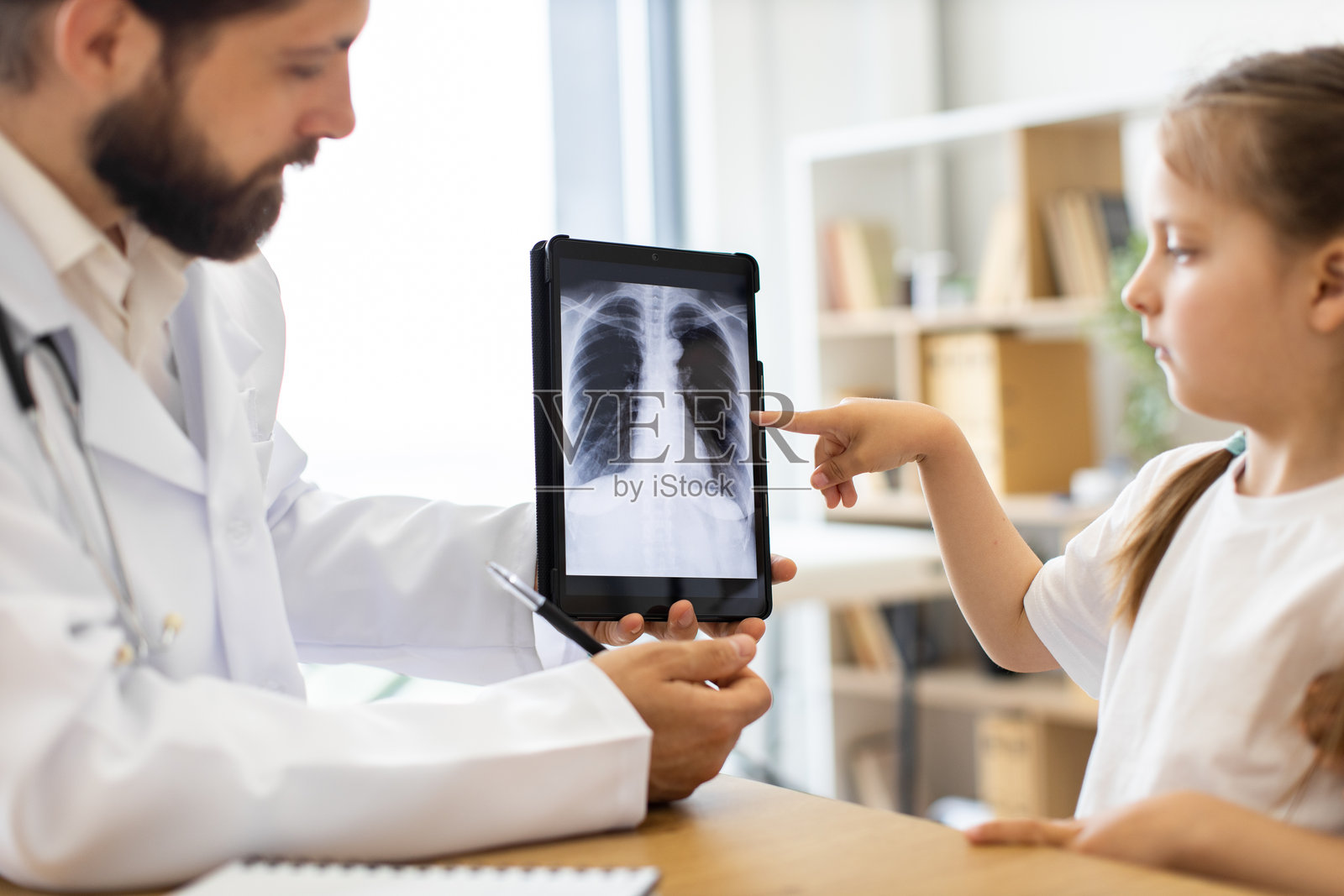 白人医生在诊所环境中向小女孩解释肺部X光片照片摄影图片