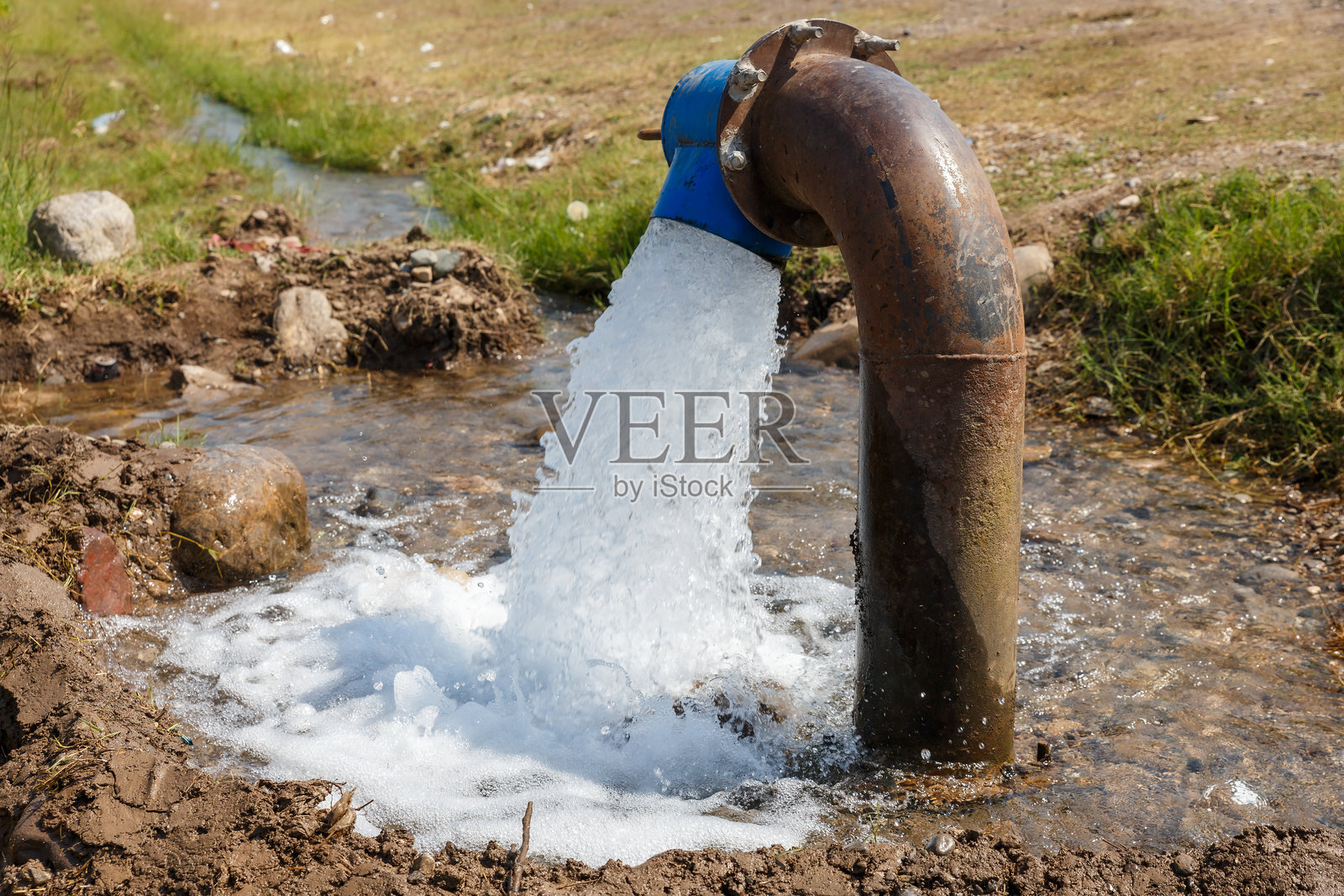 在阳光明媚的乡村地区，水从管道流入小溪。照片摄影图片