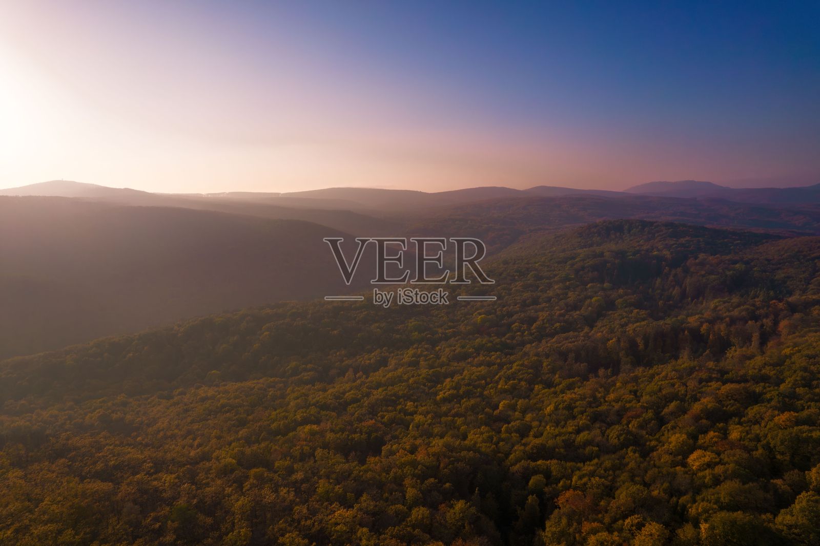 日落时分郁郁葱葱的森林和山丘的鸟瞰图。照片摄影图片