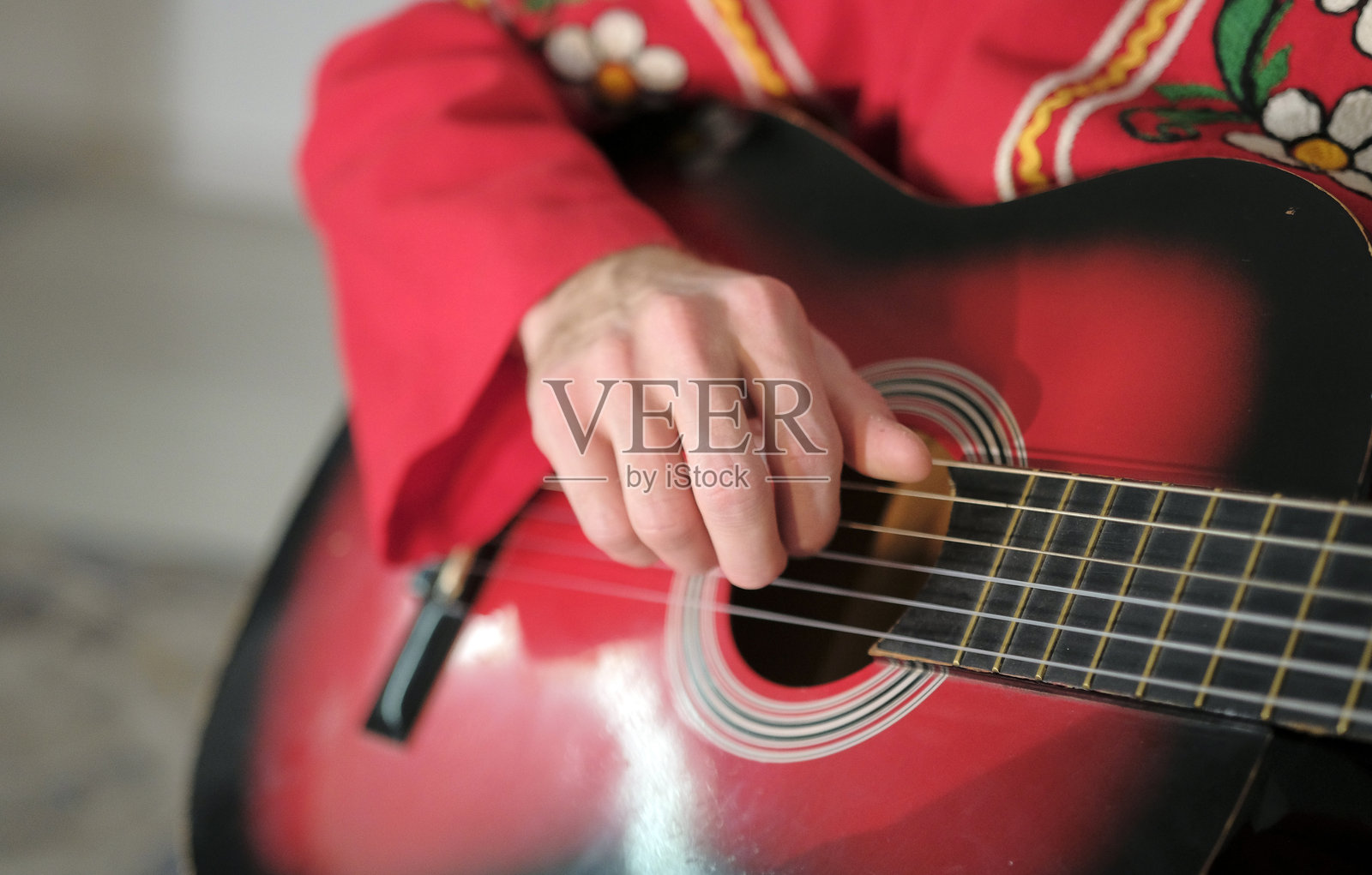 一名男子正在演奏一把红黑相间的吉他，特写镜头，聚焦于手和琴弦。经典乐器。吉他课程。照片摄影图片