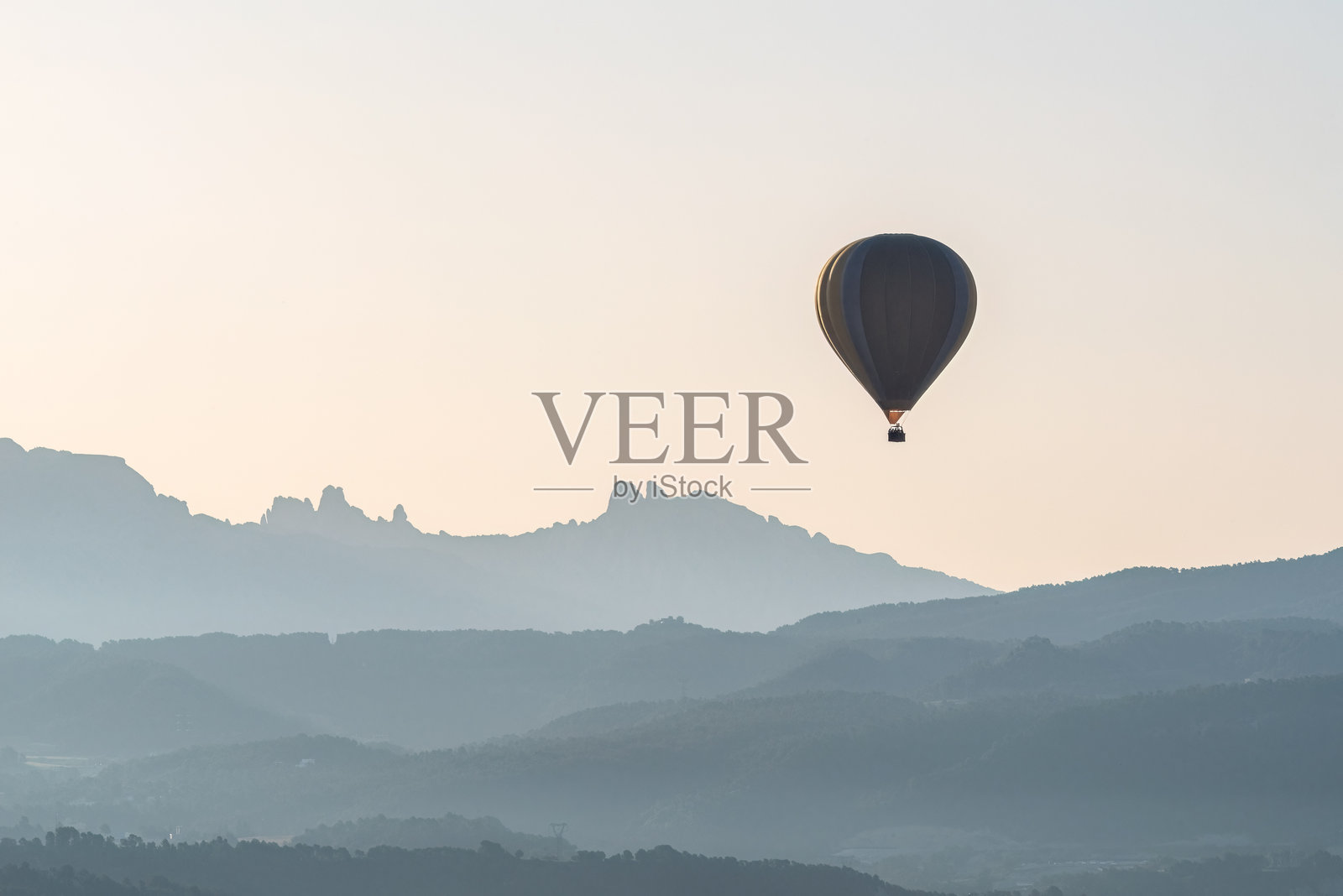 热气球在西班牙加泰罗尼亚的伊瓜拉达附近的蒙特塞拉特山脉上空宁静地漂浮，照亮了欧洲热气球节期间的黎明景观。照片摄影图片