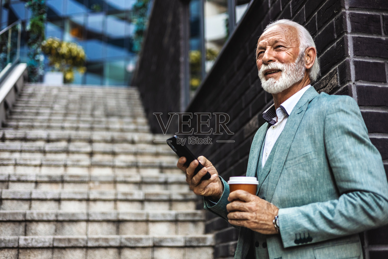 成功的白人商人在现代办公大楼外穿着西装使用智能手机，成熟的老板微笑着查看信息并在线阅读新闻。照片摄影图片