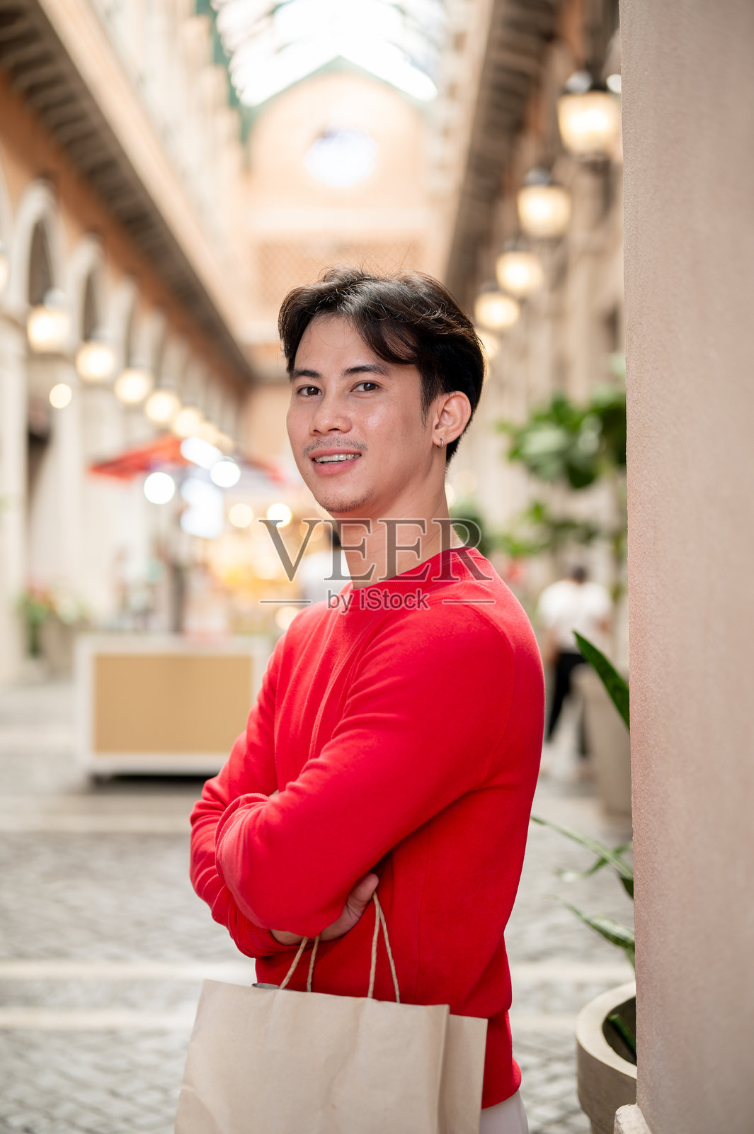 一位英俊的亚洲男子在冬季的华丽购物中心里提着购物袋。照片摄影图片