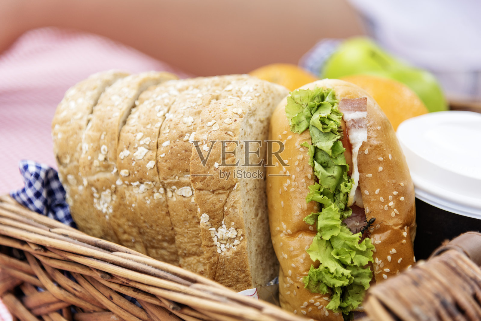 野餐篮里的食物：新鲜面包、水果、咖啡杯和橙汁，放在红色毯子上的木制柳条箱子里。小麦面包店的水果、食物和饮料，展现了绿色公园的户外生活方式。健康的早餐开胃菜盒。照片摄影图片