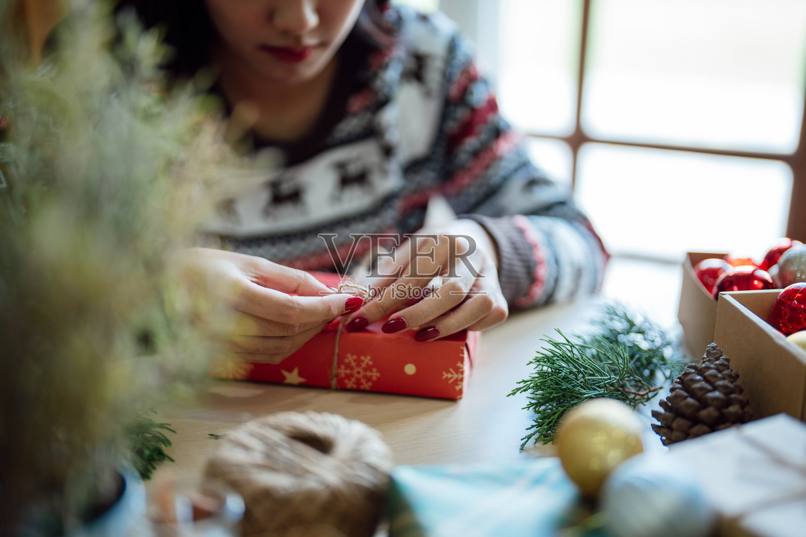 穿着针织毛衣的女人用环保纸包装圣诞礼物，女孩正在打包圣诞礼物，圣诞节假日概念照片摄影图片