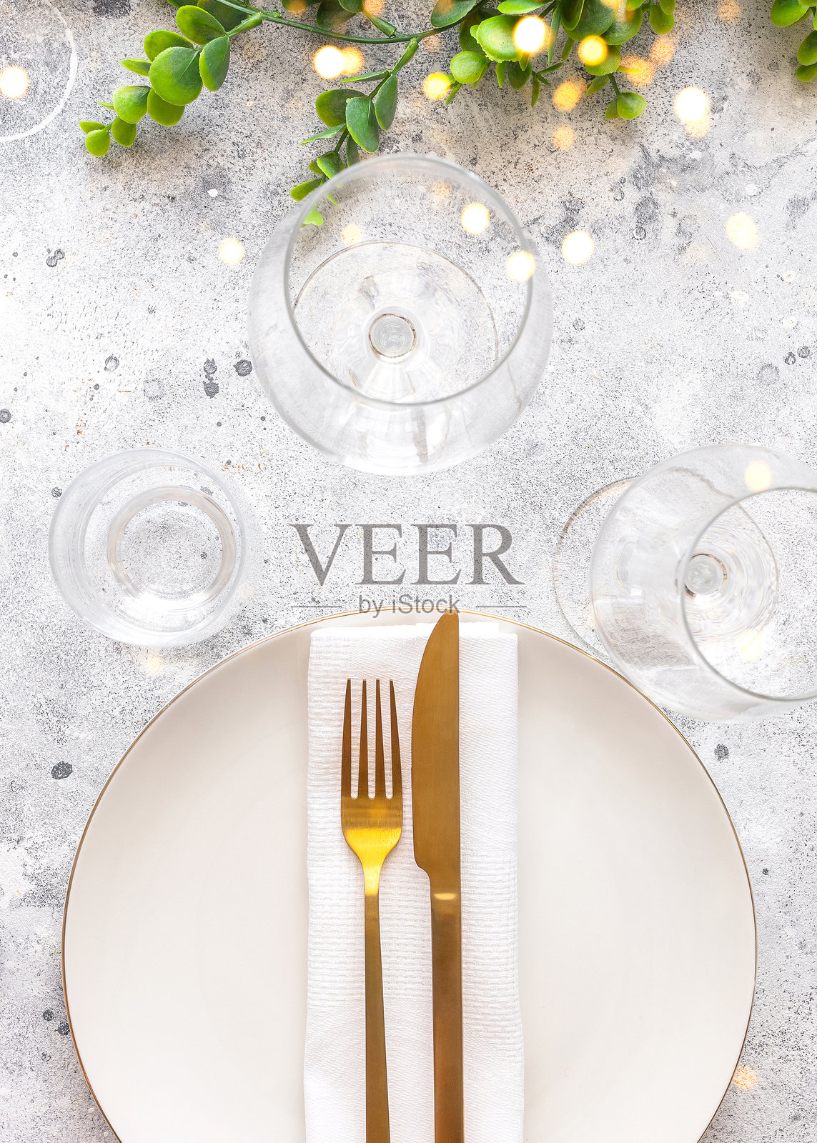 圣诞节的节日餐桌布置，白色盘子配金色餐具，酒杯和中央花卉装饰以及金色虚化效果。俯视图照片摄影图片