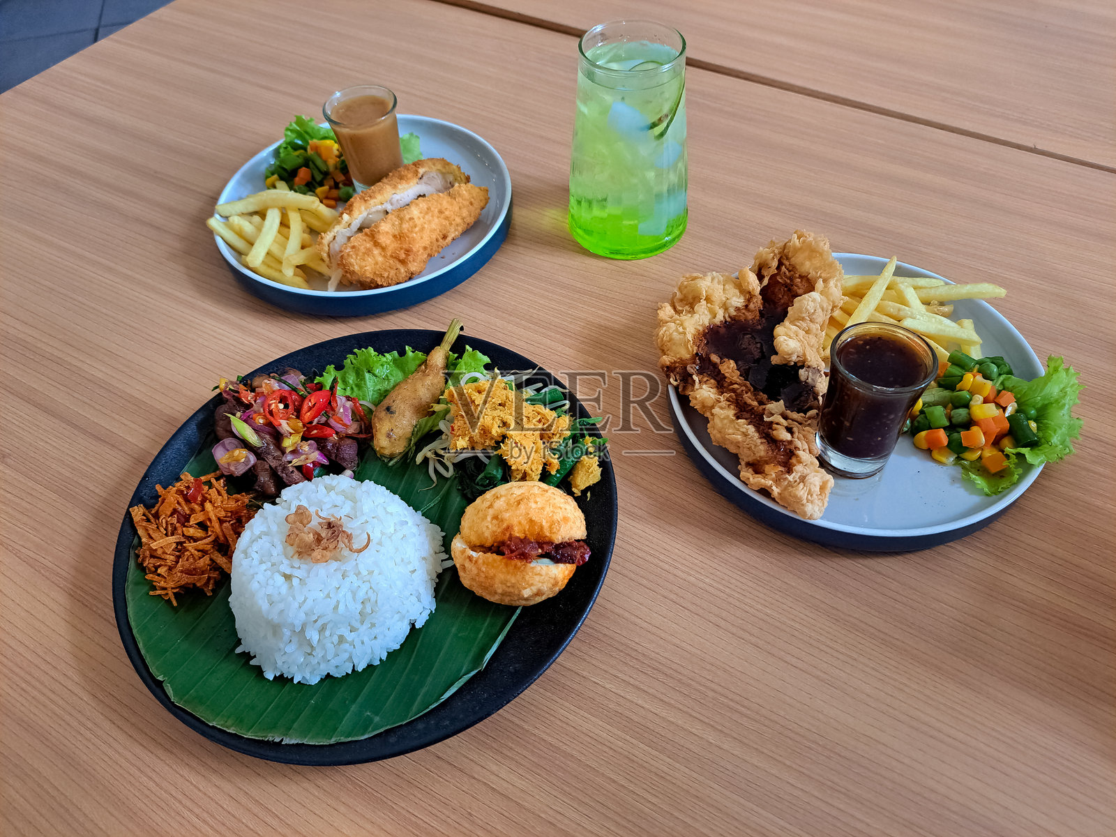 巴厘岛乌拉米饭是一道来自印度尼西亚的传统菜肴。配有脆皮鸡肉、马苏里拉蘑菇和黑胡椒牛排，搭配鸡肉片、薯条和混合蔬菜。巴厘岛冰饮或巴厘岛库乌特冰饮。食品和饮料菜单。照片摄影图片