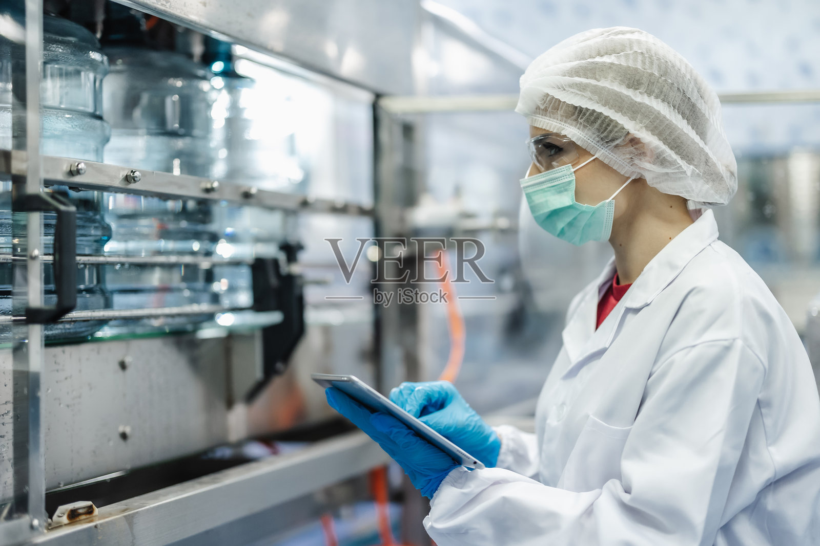 在饮用水工厂工作的工人，穿着卫生制服，保持工作场所的清洁与卫生。照片摄影图片