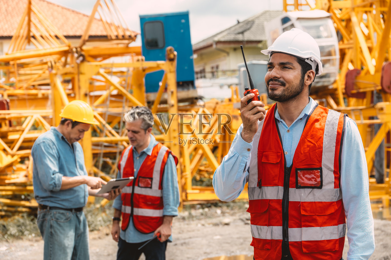 快乐的印度工人在建筑工地上控制无线电操作。工头通过对讲机指挥塔吊工作。照片摄影图片