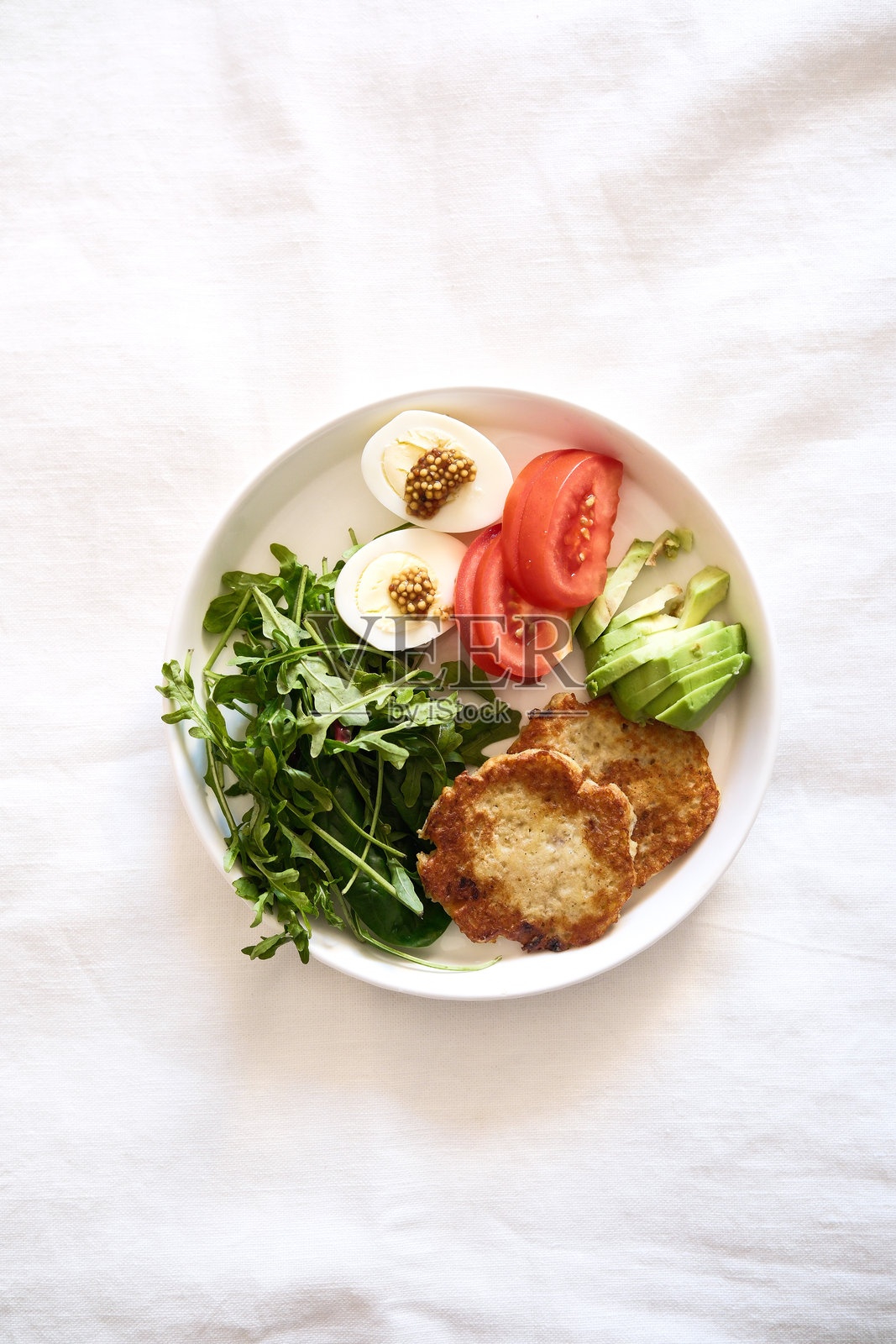 一盘色彩鲜艳的新鲜沙拉，上面有煮鸡蛋、成熟的西红柿和脆嫩的绿叶，摆放在白色布料上，倡导健康习惯。照片摄影图片