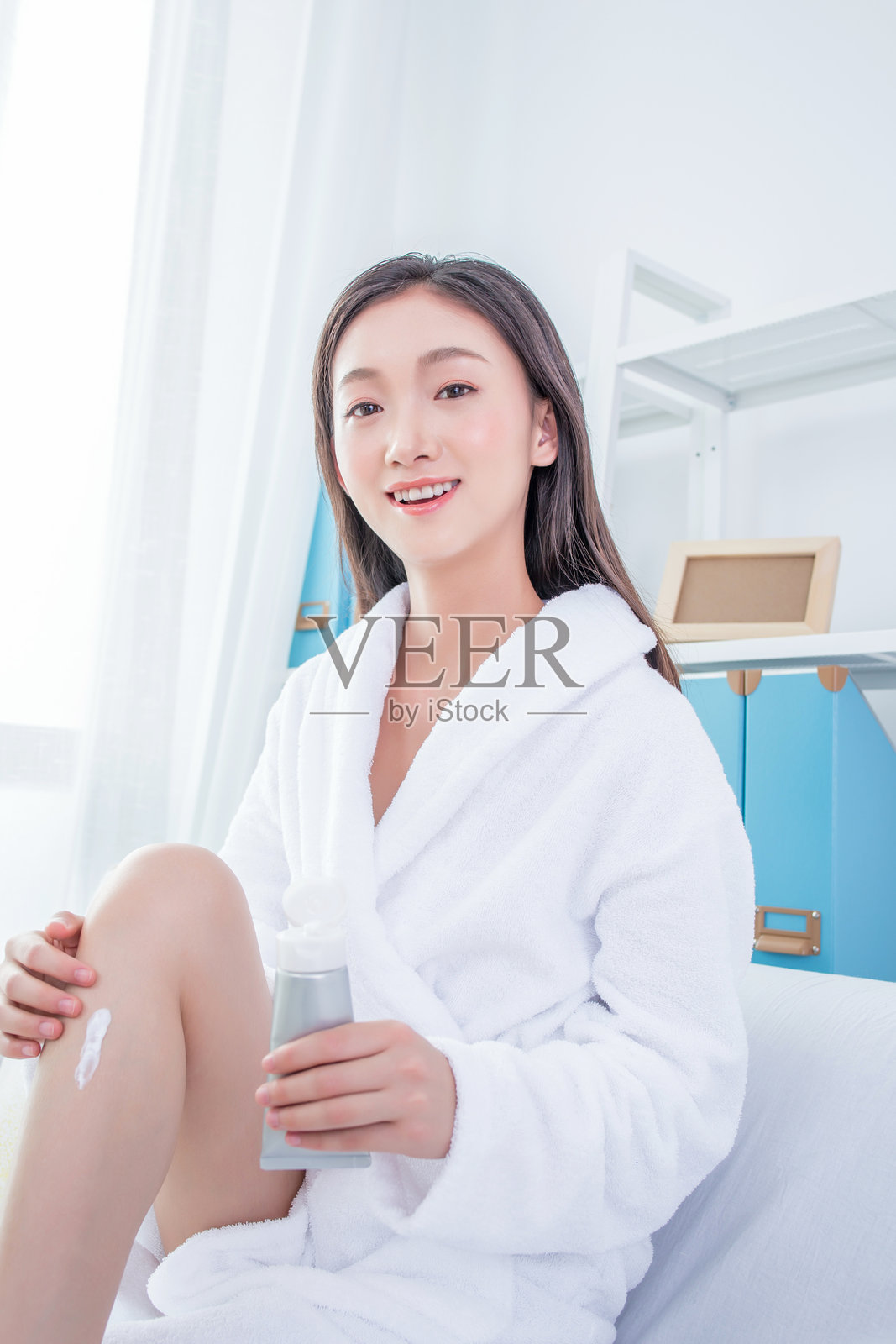 美丽的女人坐在沙发上给腿部涂抹护肤霜照片摄影图片