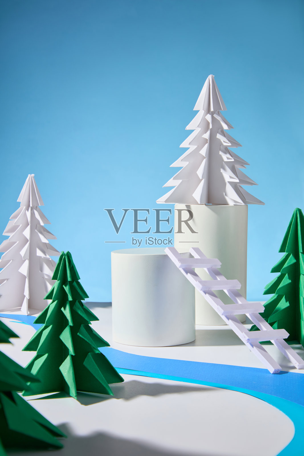 这幅图展示了冬季氛围，空的圆形产品展示平台，各种纸制松树，表面上有蓝色纸河，背景是蓝色的。照片摄影图片