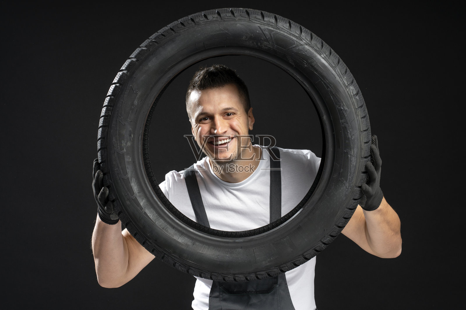 微笑的机械师在黑色背景前抱着一个轮胎照片摄影图片