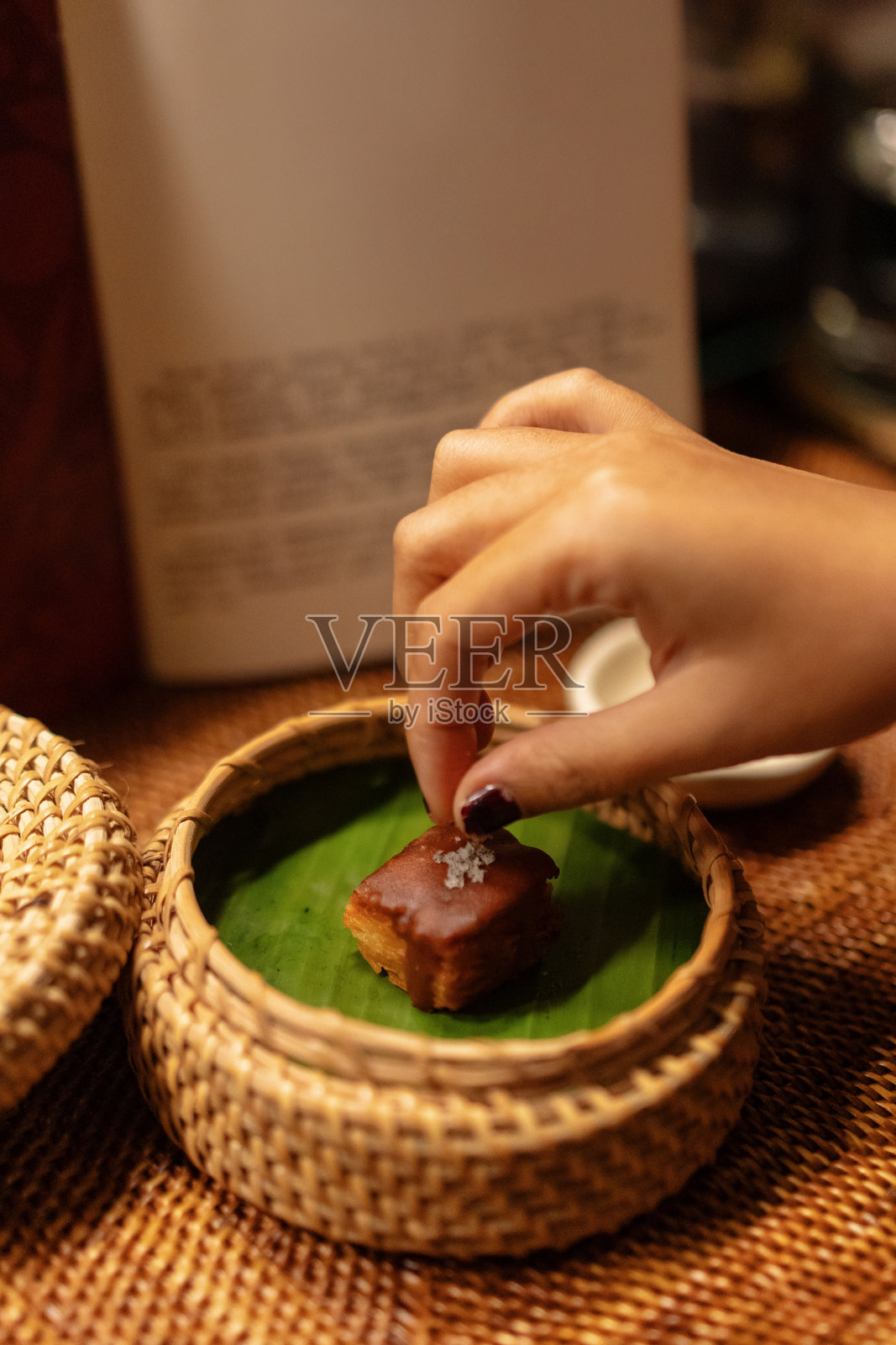 女性手部特写，将海盐撒在香蕉叶上的甜点小吃上，放在藤编篮子里。照片摄影图片