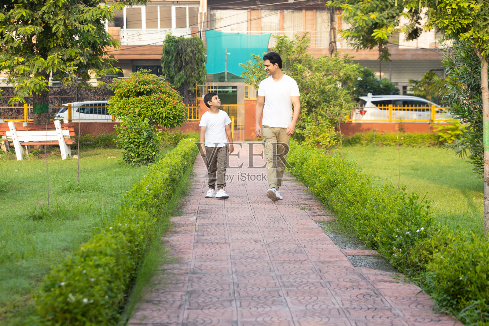 年轻的印度父亲在夏季公园里与他的小儿子散步，共度时光。父亲身份和育儿理念。照片摄影图片