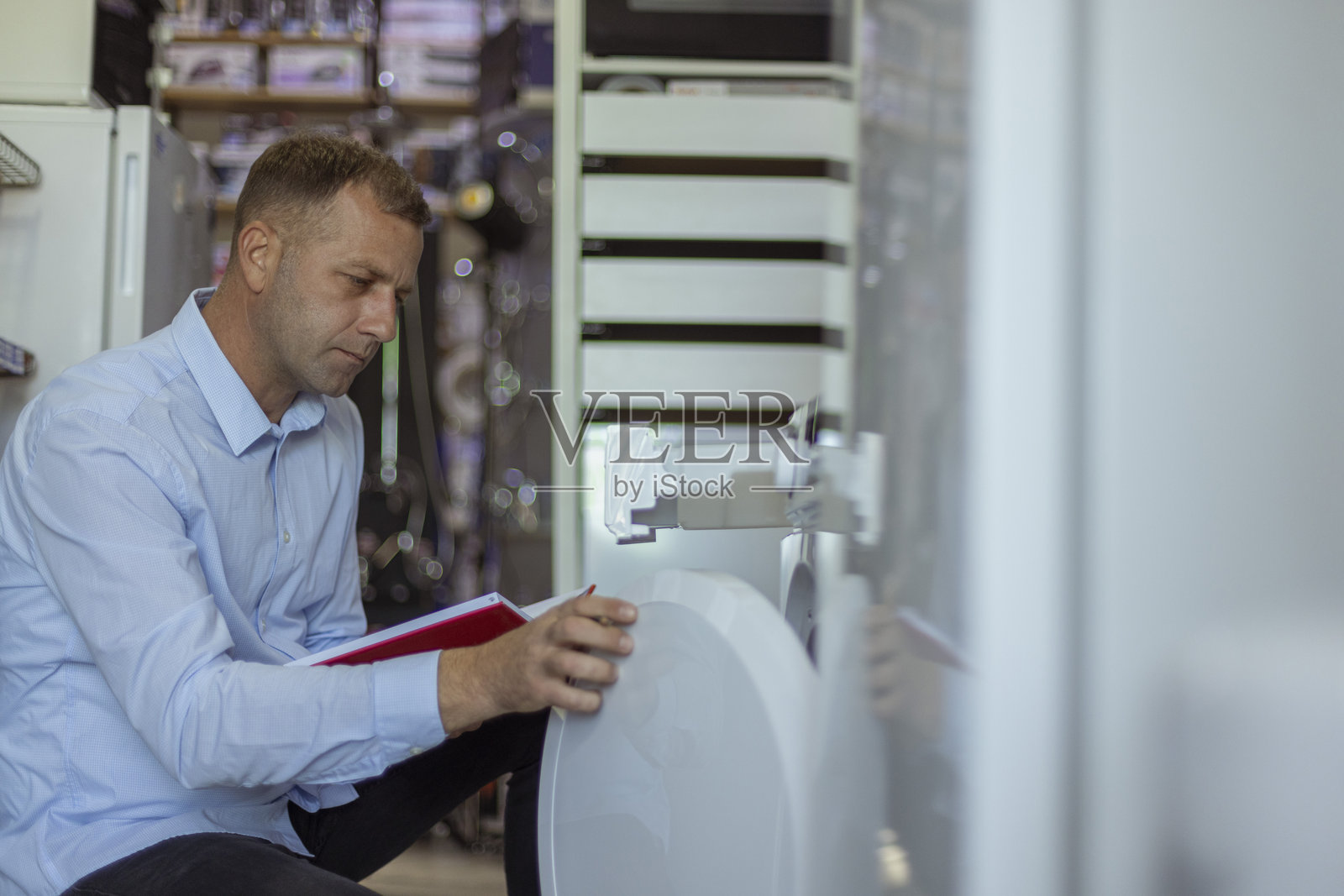 男性家电商店老板打开洗衣机，并在笔记本上记录该设备的特点。照片摄影图片