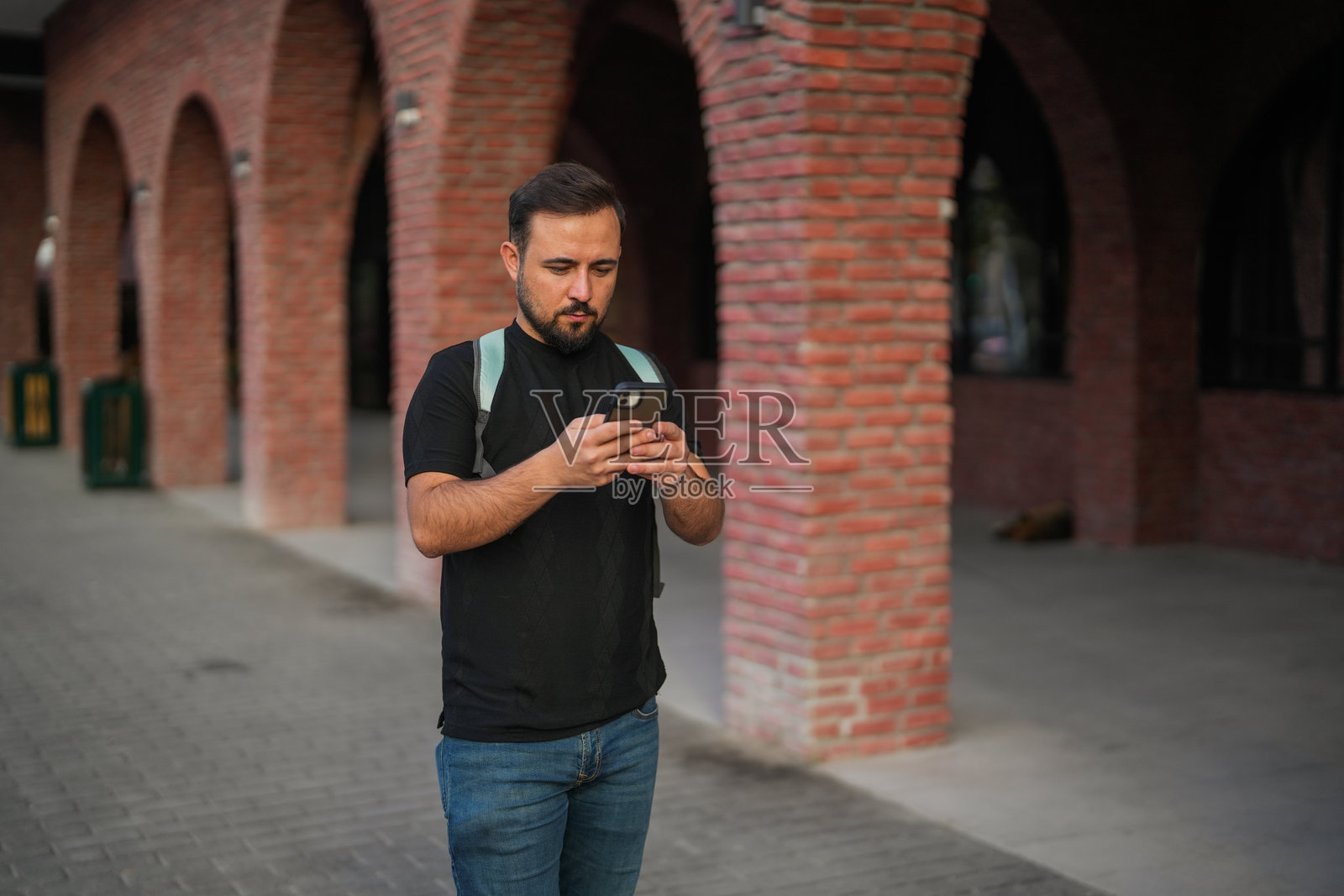 男子在市中心的街道上走着，低头看着手机。照片摄影图片