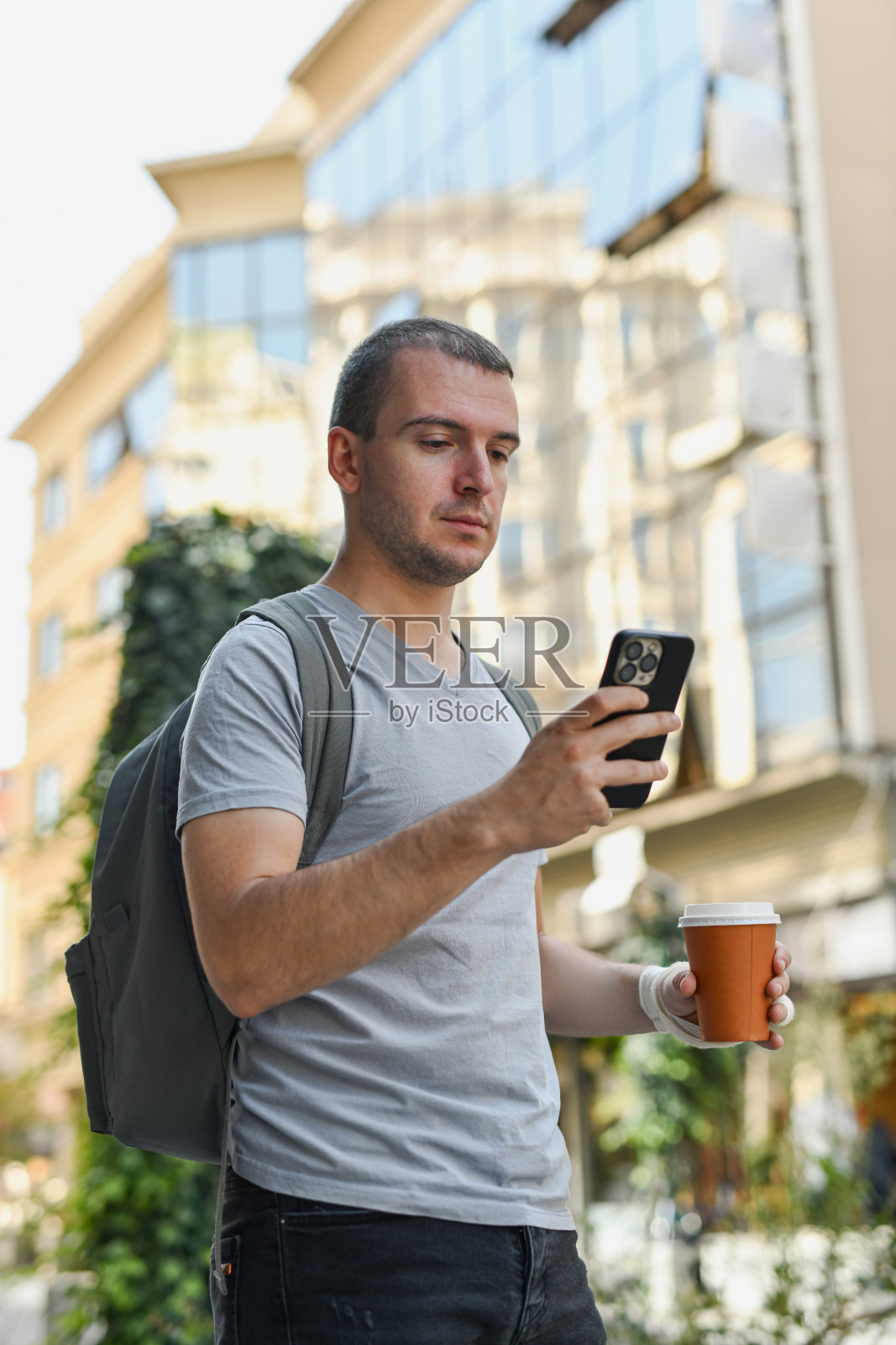 年轻男性在街上走着，手里拿着咖啡杯，同时在网上支付。照片摄影图片
