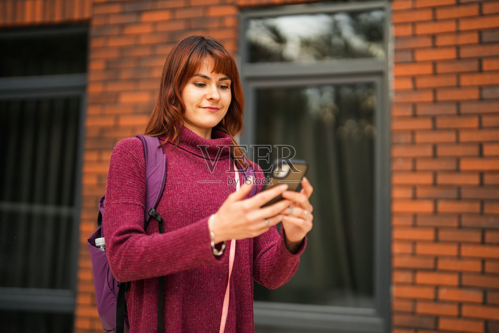 年轻美丽的女性在红色背景前看着手机照片摄影图片