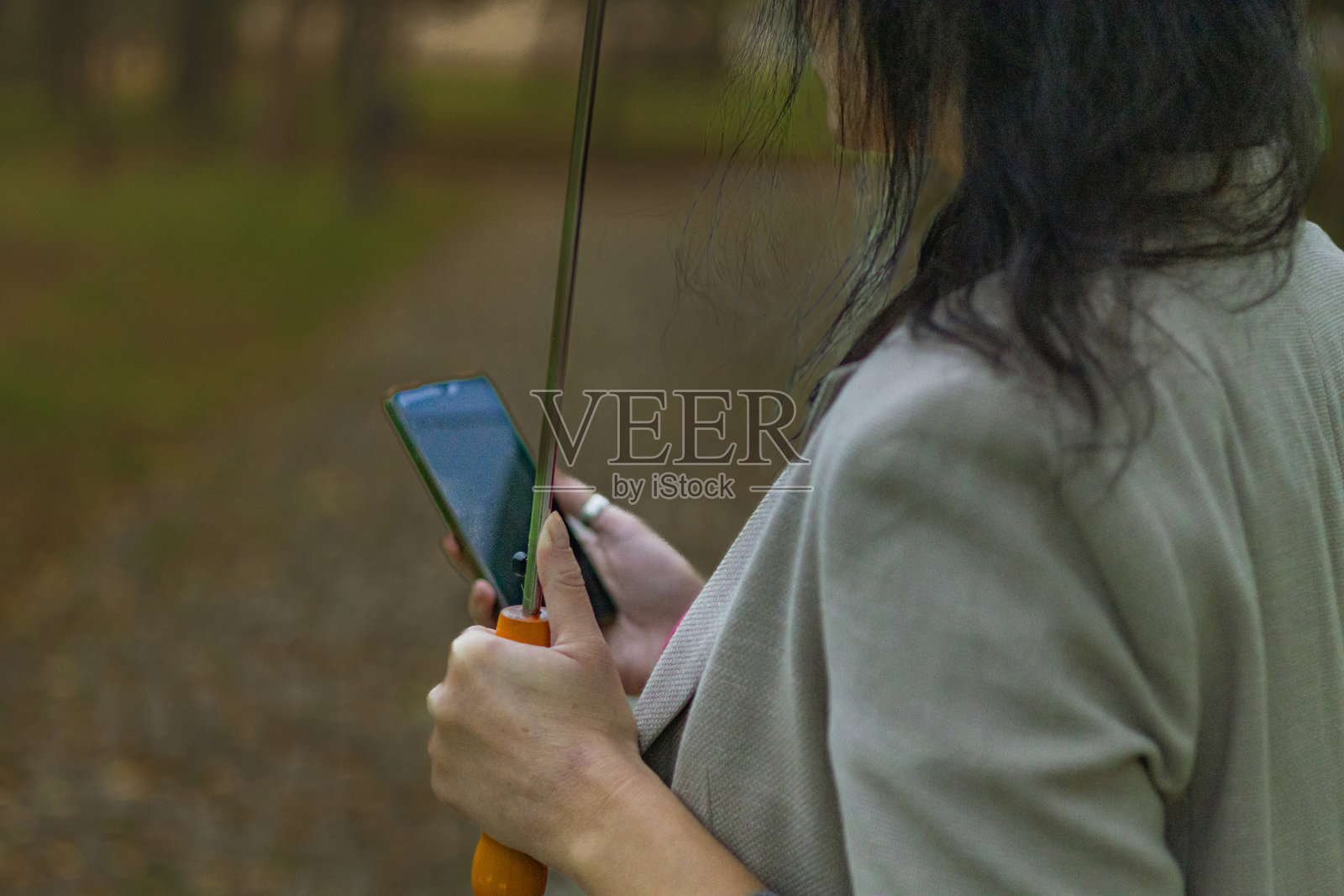 中年女商人在秋天的公共公园里，雨天使用手机进行电子银行或投资，手里还撑着伞。照片摄影图片