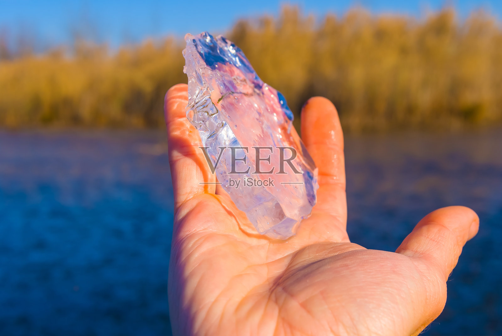 男人手中握着一块冰，站在湖岸边。照片摄影图片