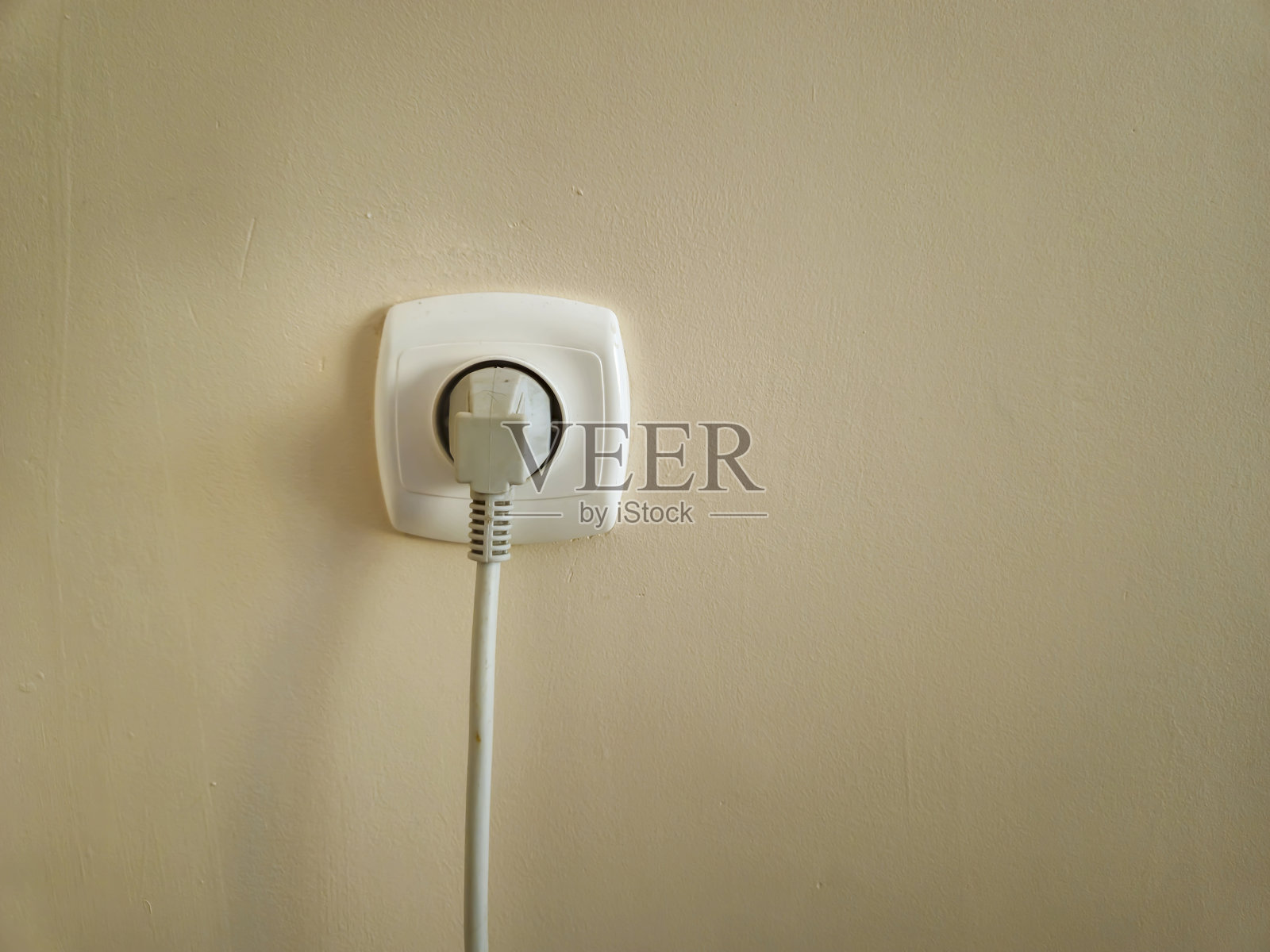 插座特写，插头插入其中，背景为简单的浅色墙壁。适合家庭、能源或科技主题。照片摄影图片