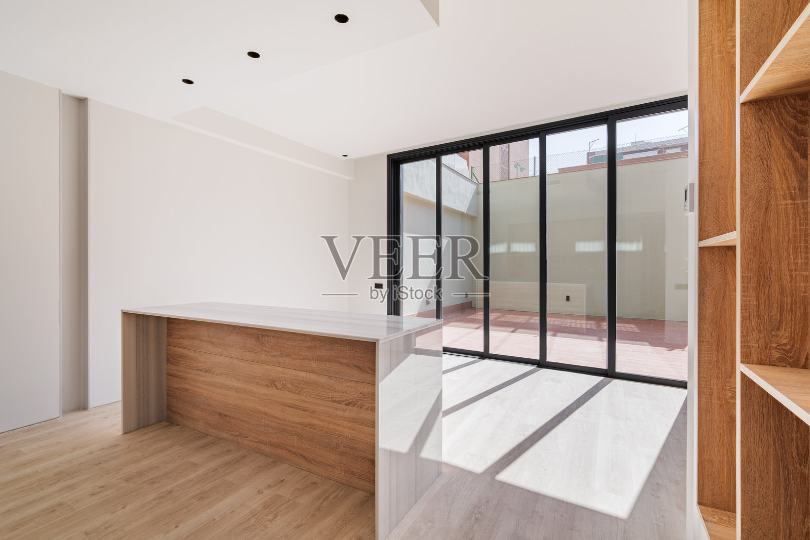 翻新公寓的空荡荡的室内，阳光透过大窗户洒入。现代厨房配有岛台和木质家具。照片摄影图片