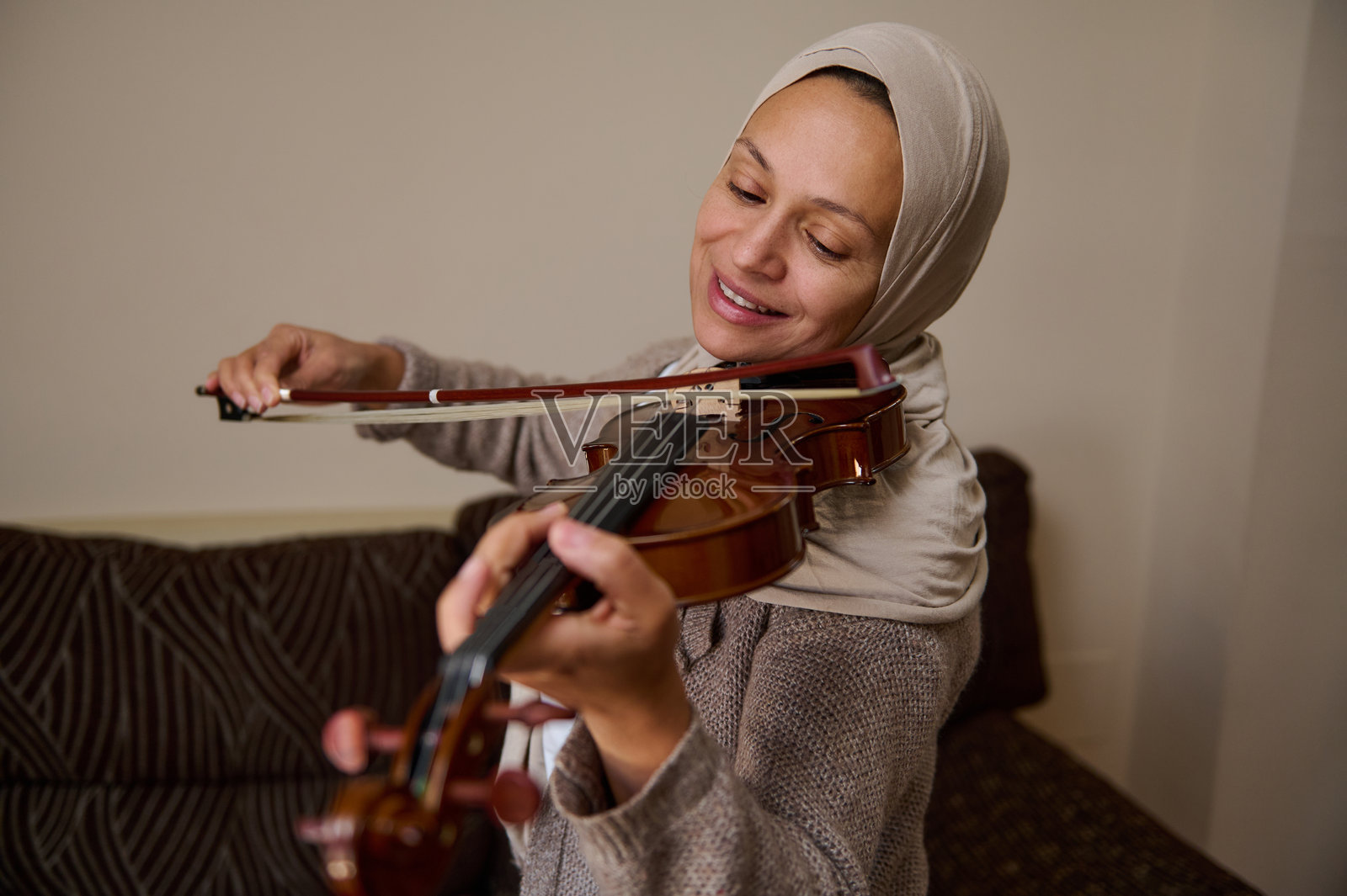 女人在室内愉快地拉小提琴，脸上洋溢着满足的微笑照片摄影图片