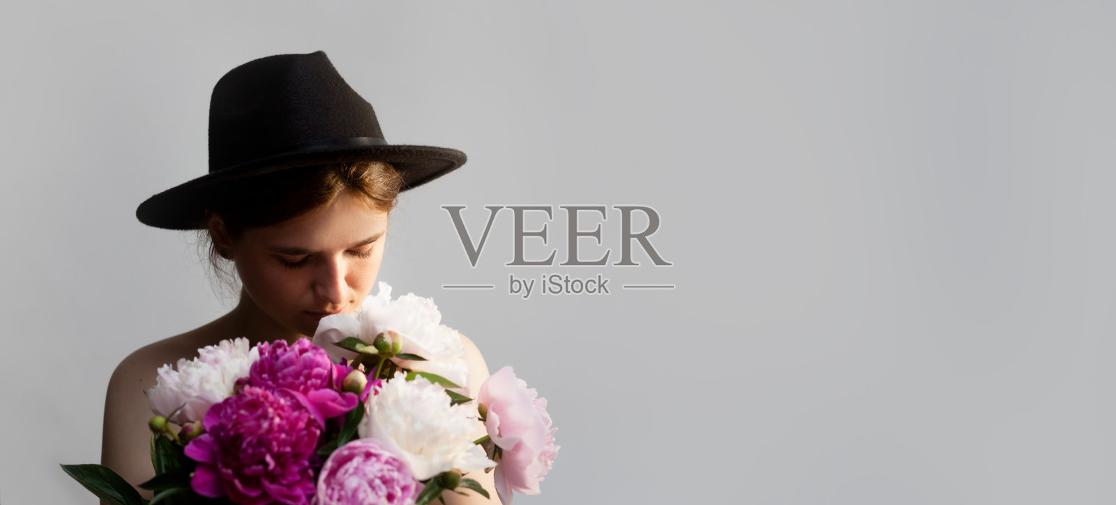 一幅时尚的横幅，展示了一位年轻女性，身上装饰着精致的牡丹花，背景为柔和的灰色。适合设计的横幅，留有空白区域。照片摄影图片