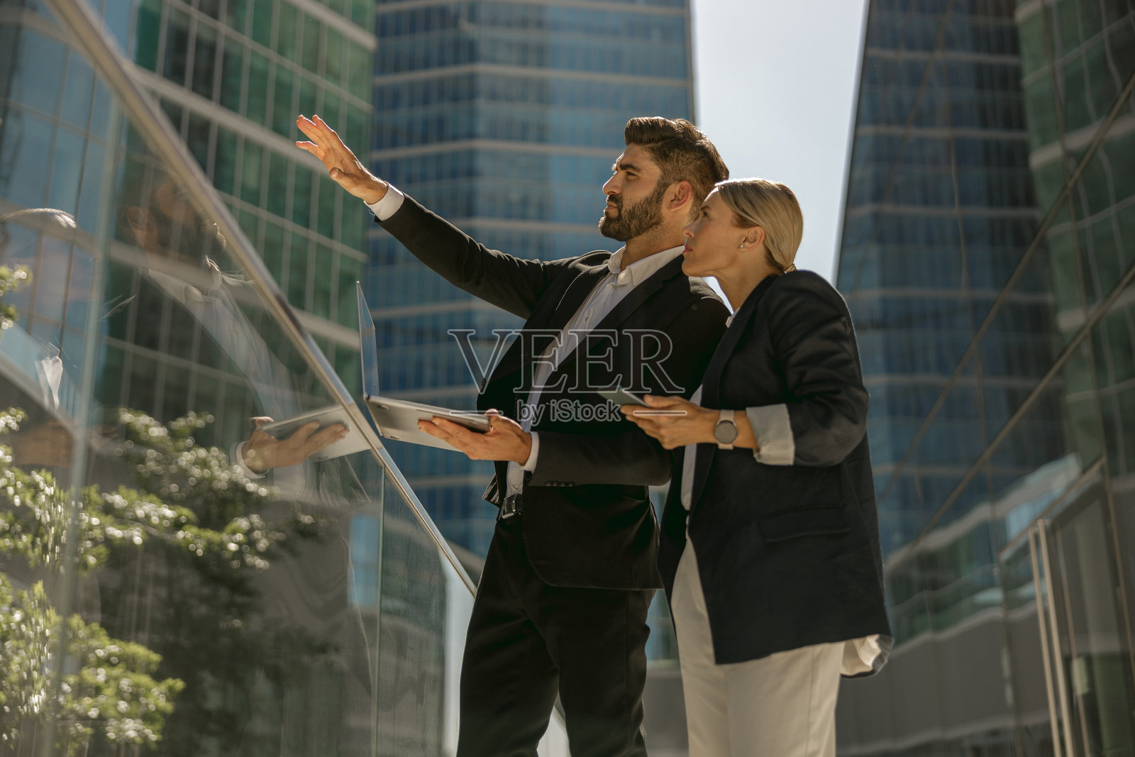 商人拿着笔记本电脑站在办公室阳台上给女同事看东西照片摄影图片