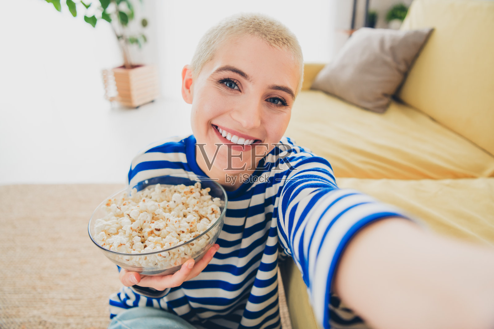 年轻女性穿着条纹毛衣，微笑着在家享受休闲时光，手里拿着爆米花。照片摄影图片