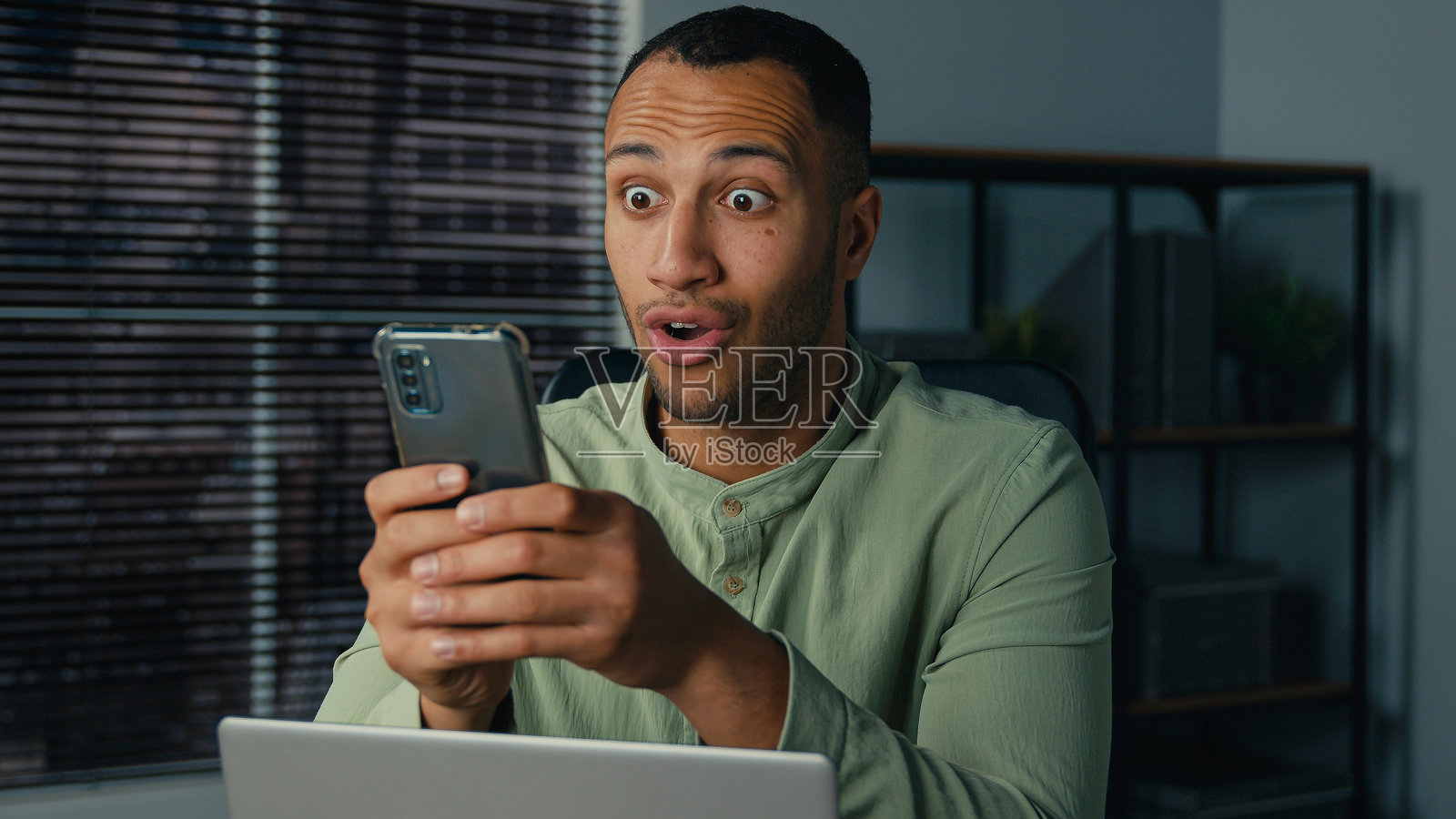 兴奋的非裔美国商人收到手机上好消息的电子邮件，喜悦的男人，赢家，企业家坐在办公室庆祝在线胜利，享受互联网成功。照片摄影图片