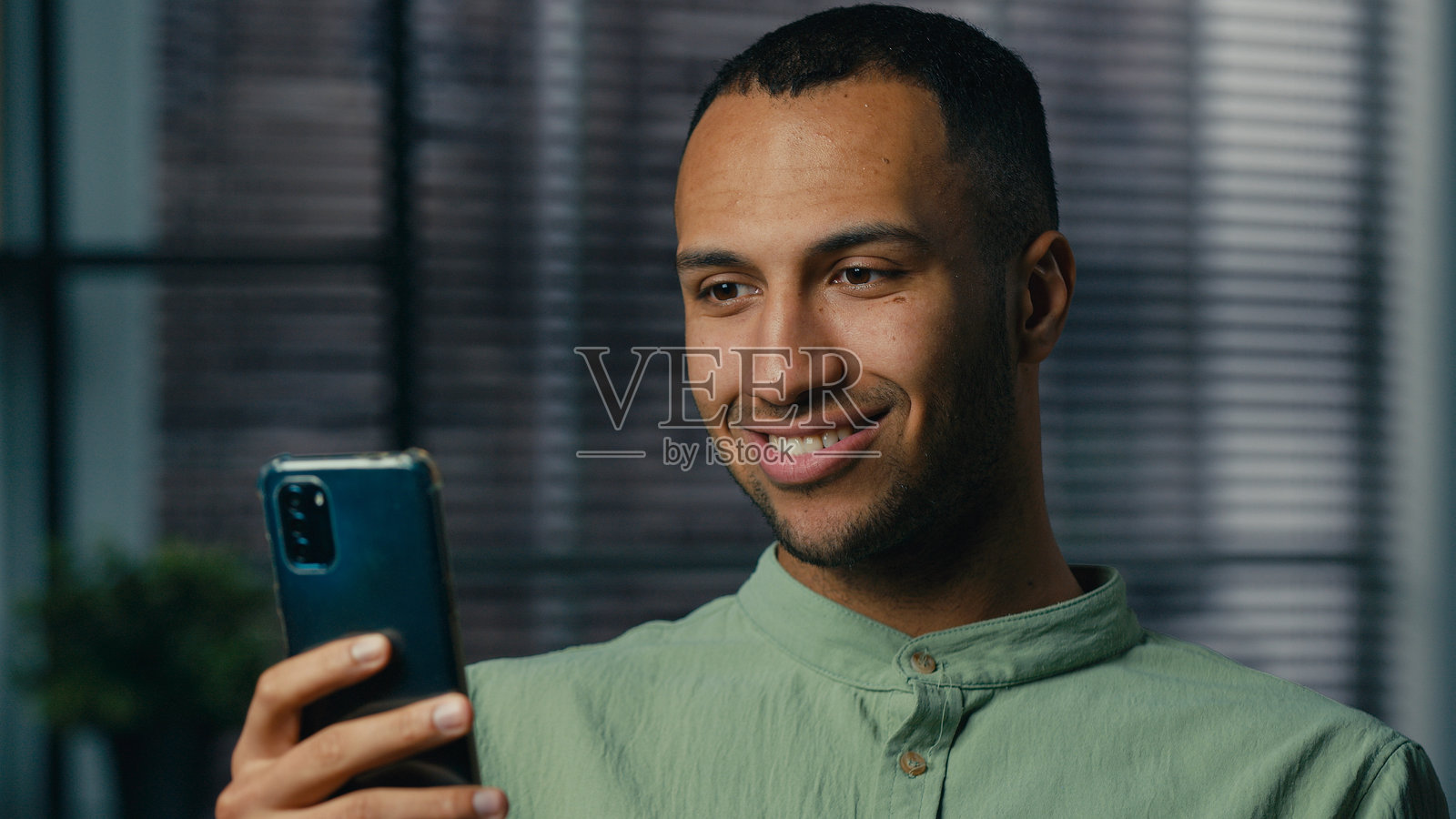 微笑的非洲裔美国商人企业家看着手机屏幕，阅读社交媒体上的好消息，快乐的男人通过手机应用接收信息，观看互联网视频，在线聊天。照片摄影图片