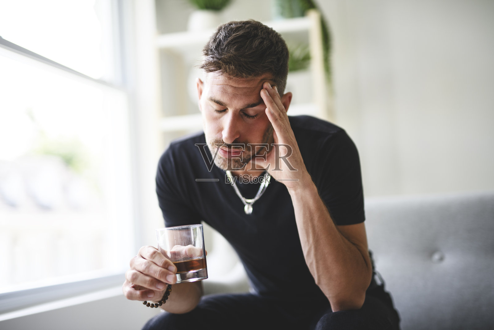 孤独抑郁的男性在家沙发上喝酒。酒精成瘾的治疗，遭受酗酒问题的困扰。照片摄影图片