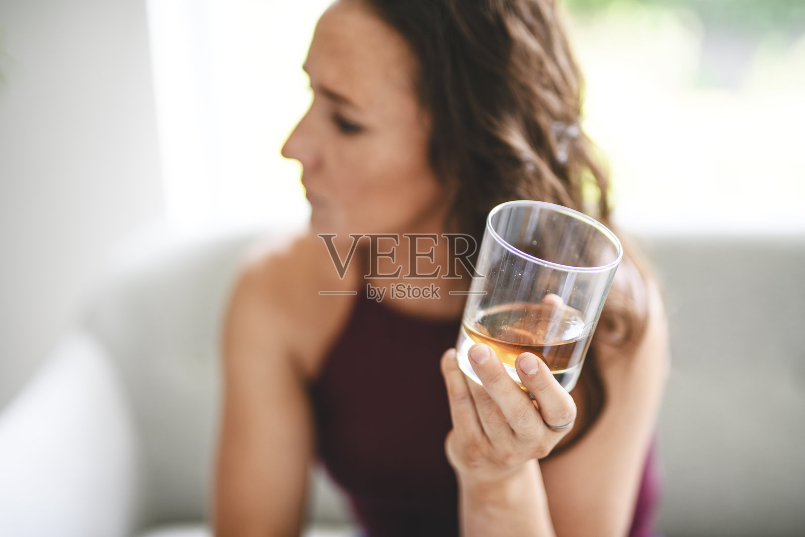 孤独抑郁的女人在家沙发上喝酒。酒精成瘾的治疗，遭受酗酒问题的困扰。照片摄影图片