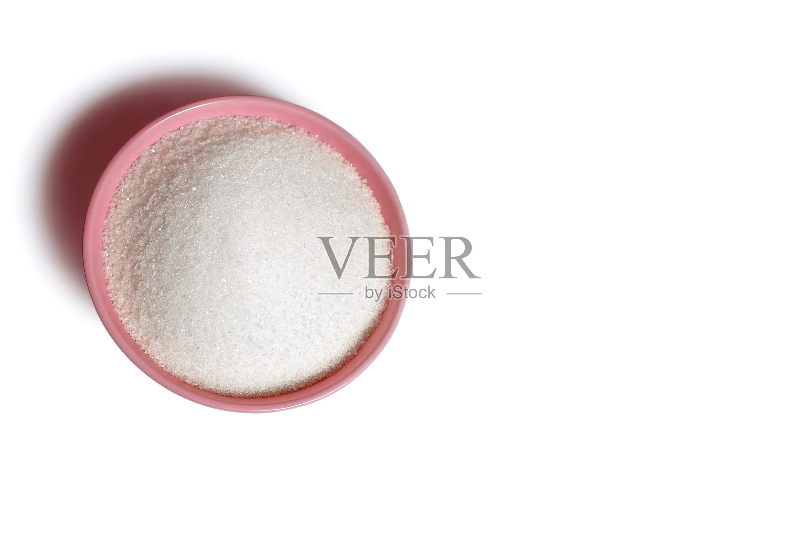 粉色深盘上放着白糖，背景为纯白色。照片摄影图片