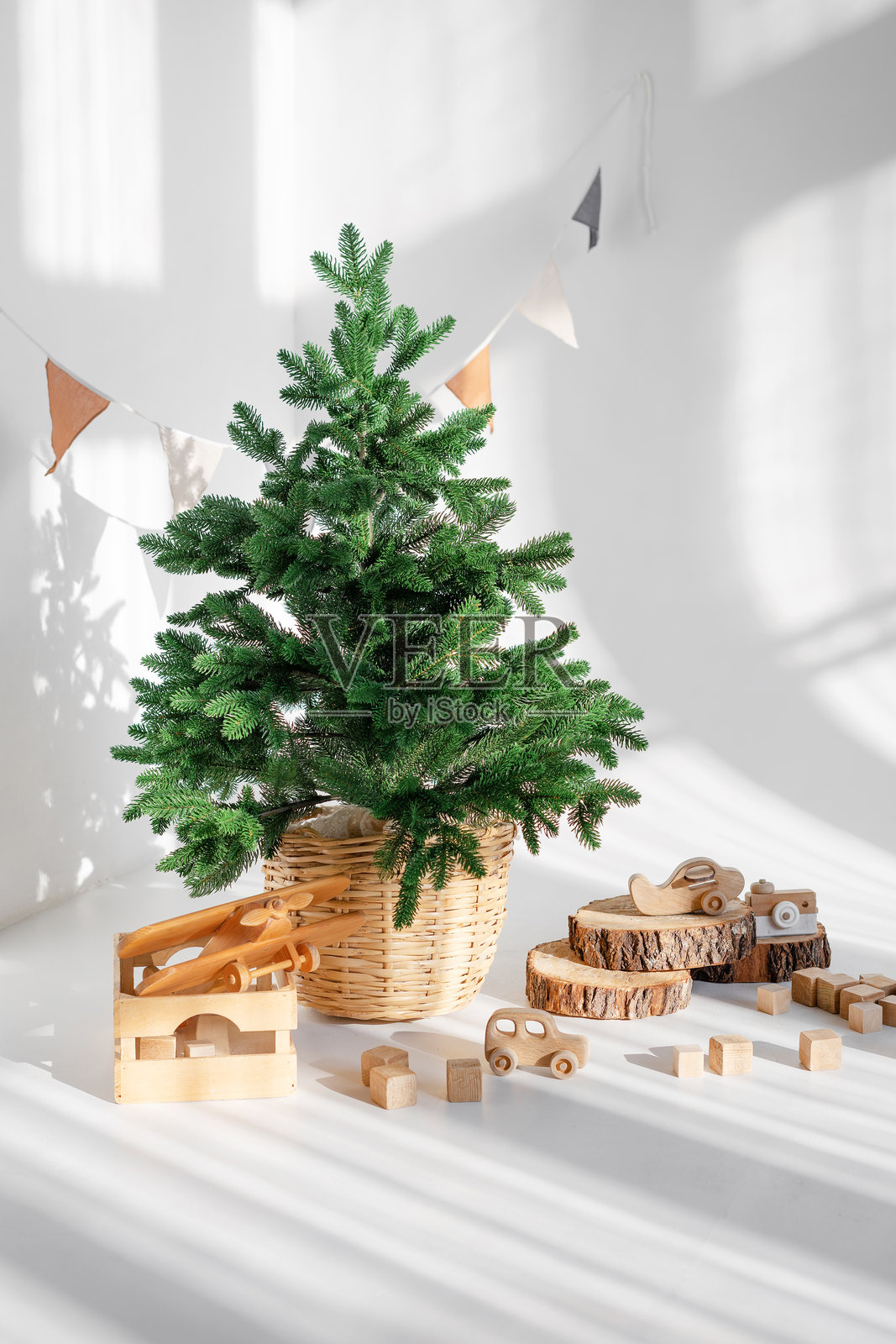 一个小型圣诞常青树放在编织的篮子里，旁边是木制玩具和木片，营造出一个温馨舒适的氛围，阳光明媚的房间里充满了光线。照片摄影图片