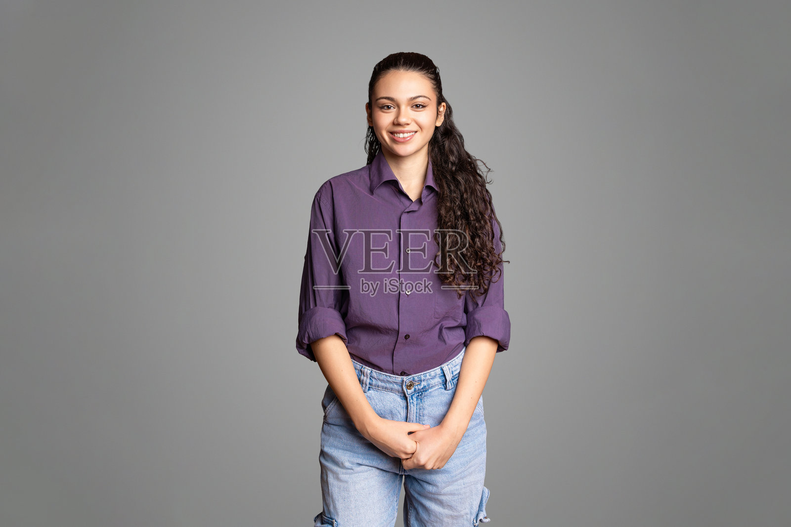 一位年轻的快乐西班牙裔女性在灰色背景下自信地微笑的工作室肖像照片摄影图片