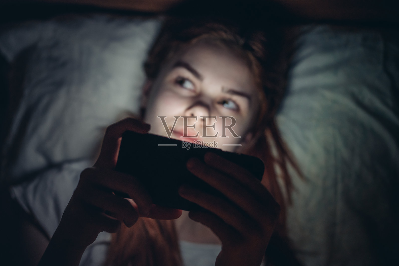 晚上躺在床上，手里拿着手机的女性，沉迷于网络。照片摄影图片