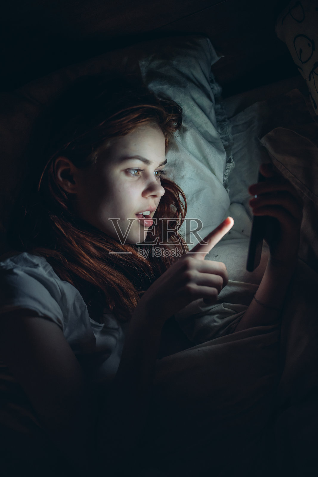 晚上躺在床上的女性手持手机，展现生活方式照片摄影图片
